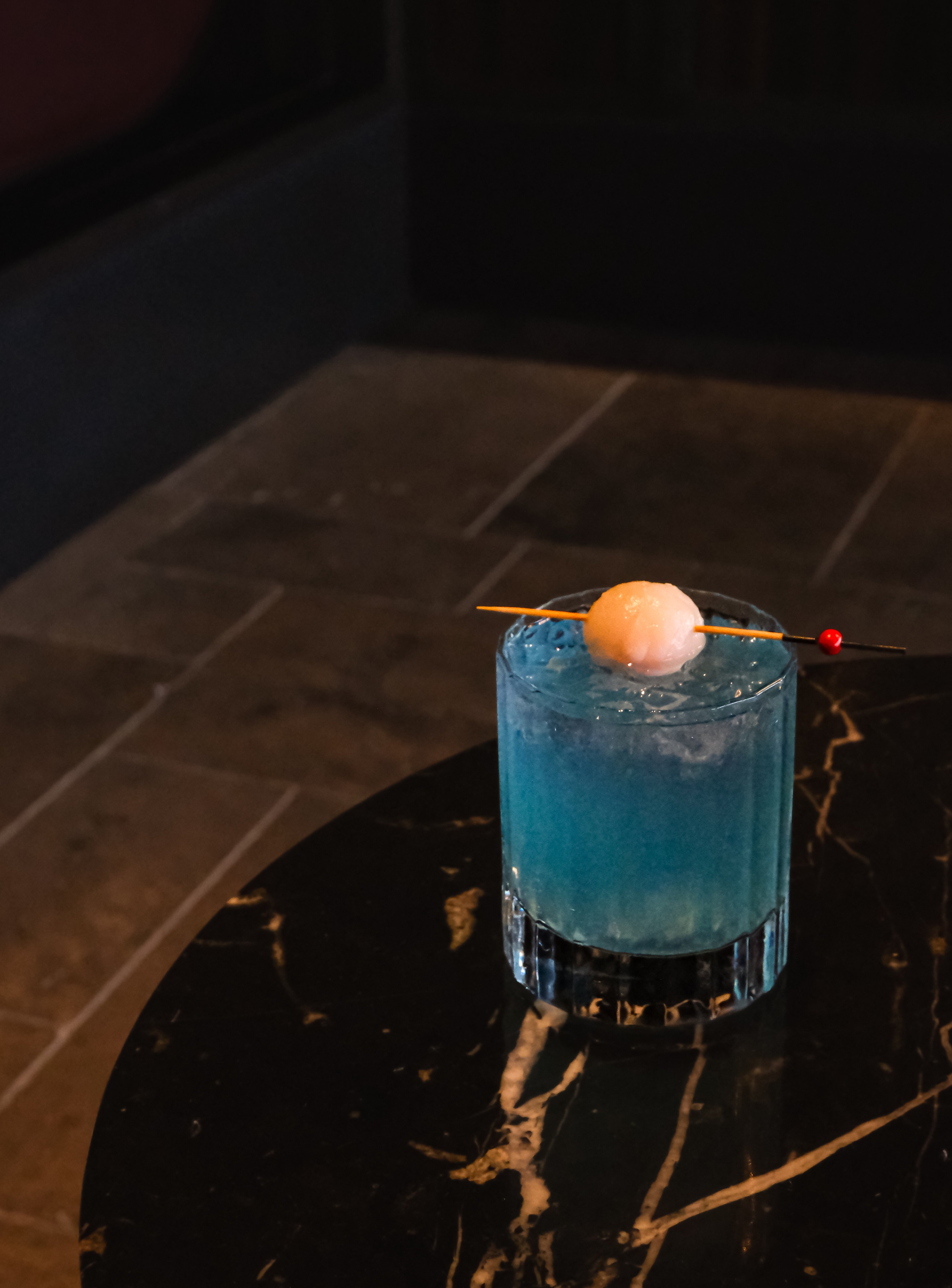 Sapphire Silk — blush-blue cocktail with skewered lychee garnish
